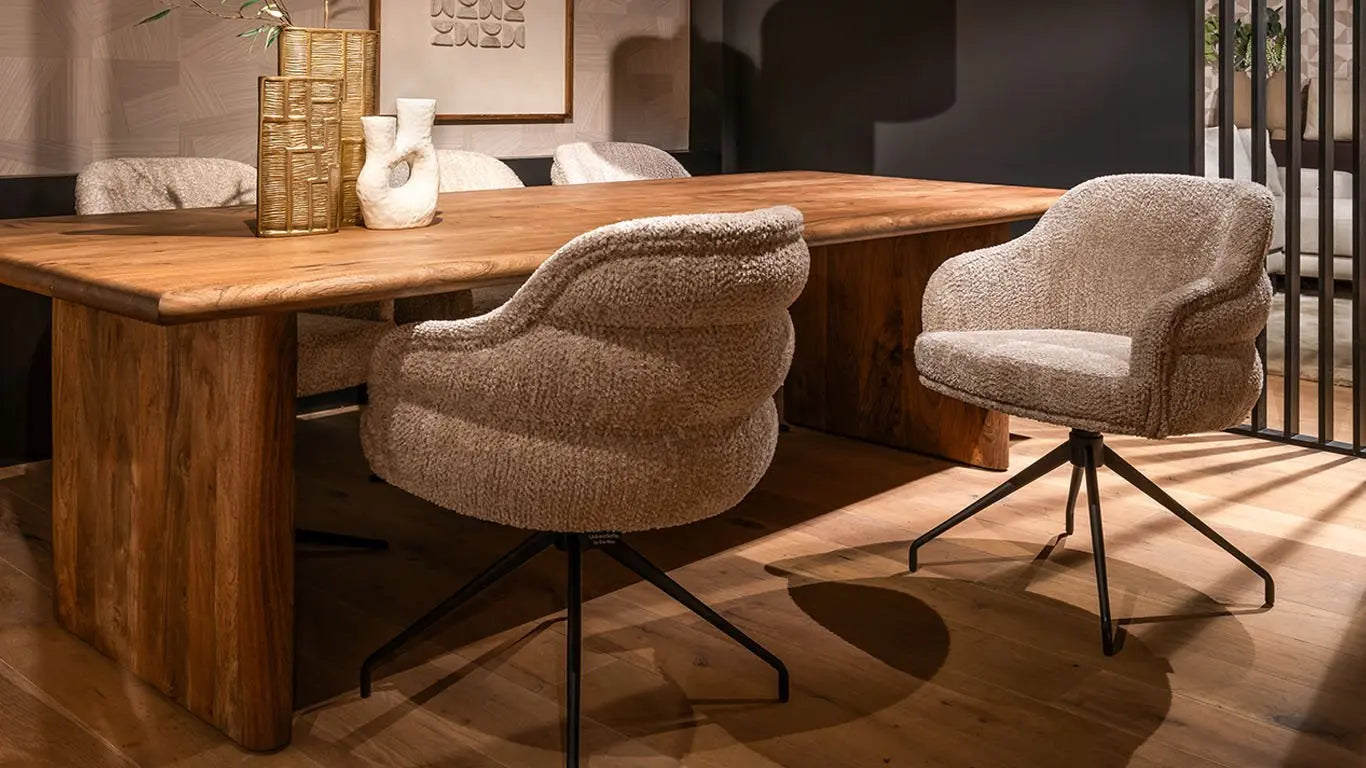 Elegante grijze stoel met gestikt fluwelen bekleding en zwarte metalen poten, geplaatst in een lichte en natuurlijke eetkameromgeving naast een groot raam.